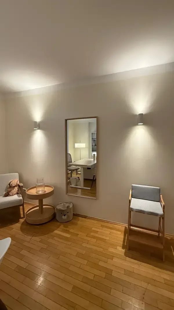 Behandlungsraum mit Wandspiegel, Sessel und kleinem Tisch